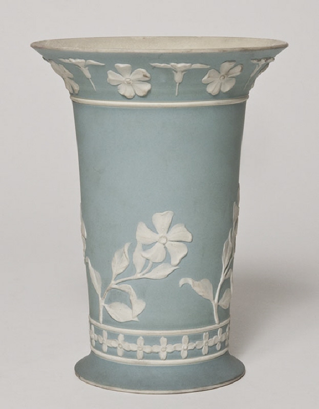 Vas, cylindrisk med utvikt fot och mynning, dekor av blommor och bårder i vit relief mot ljusblå fond