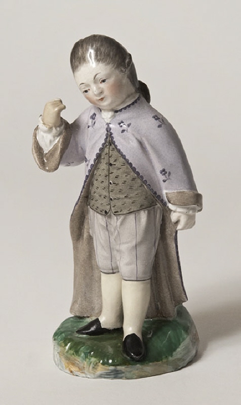 Figurin av fajans föreställande en gosse som står på en rund, grön fotplatta