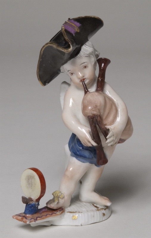Figurin, bevingad putto blåsande säckpipa
