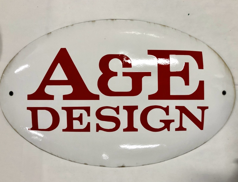 Emaljskylt, elliptisk, vit med röd text ”A&E Design”